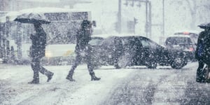 Busy and snowy city street with pedestrians walking by and vehicles behind